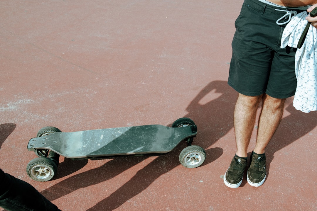 Personne en short noir debout sur sol rouge avec skate électrique